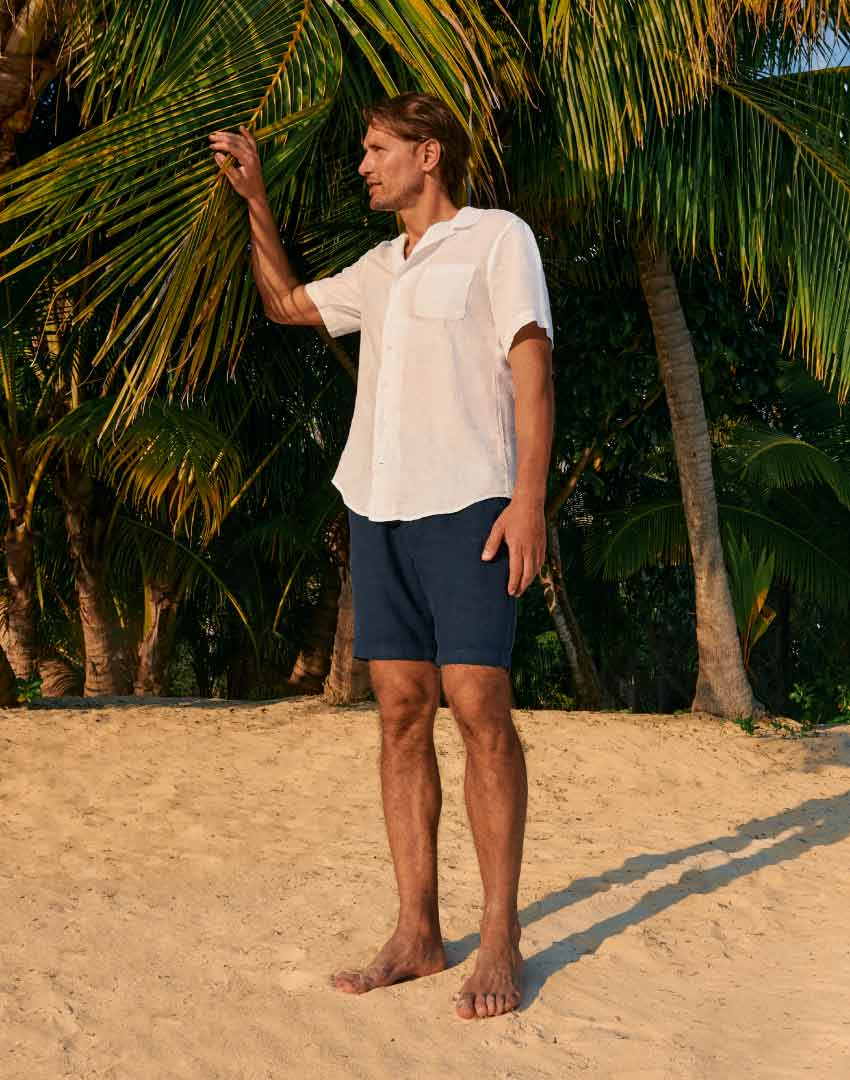 model wears mens white linen shirt and blue shorts